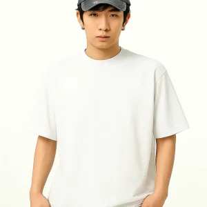 A young East Asian man wearing a plain white oversized T-shirt, a distressed dark gray baseball cap, and gray jeans, standing against a light background with a neutral expression.