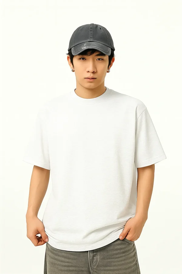 A young East Asian man wearing a plain white oversized T-shirt, a distressed dark gray baseball cap, and gray jeans, standing against a light background with a neutral expression.